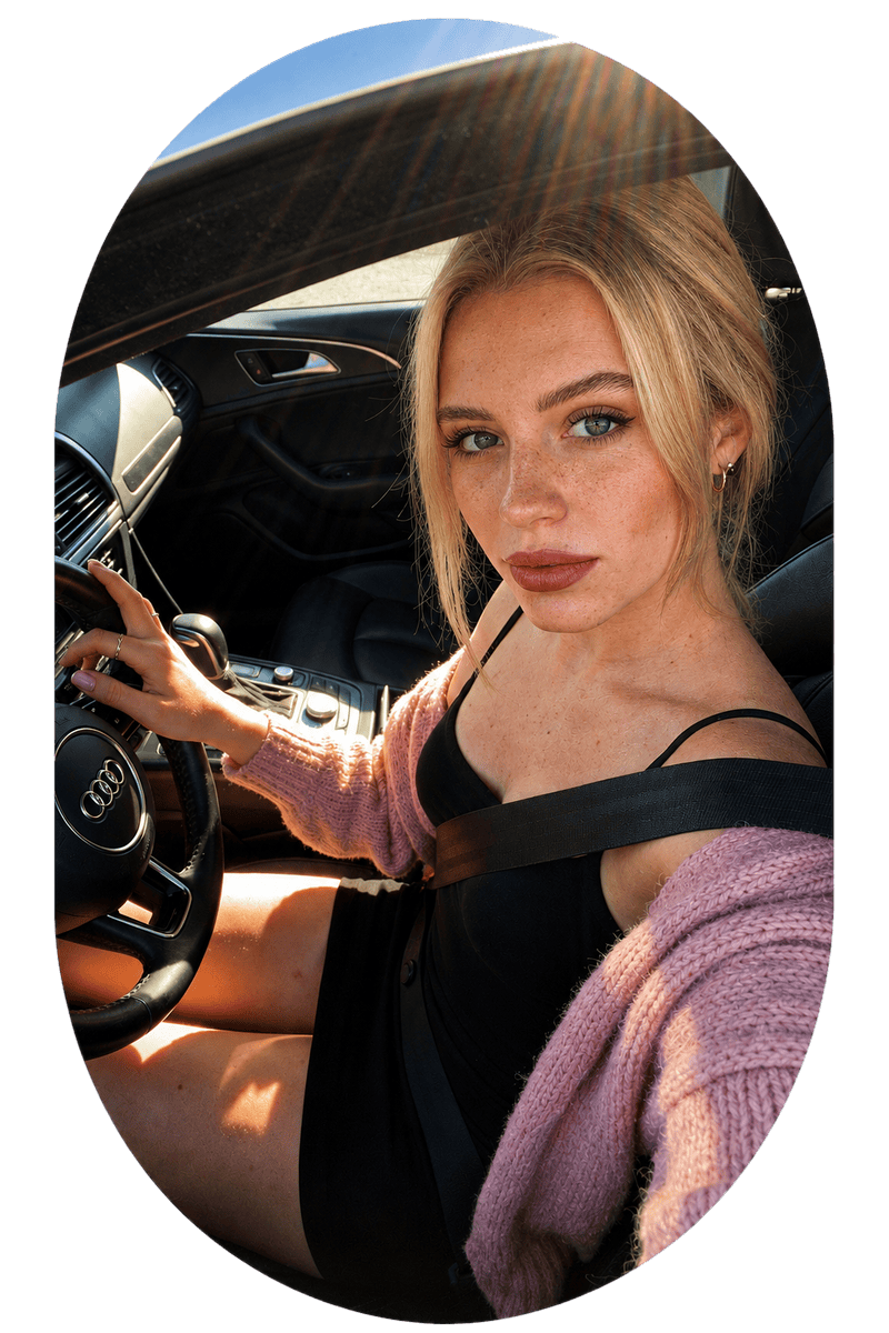 A close-up portrait of a blonde woman sitting behind the steering wheel of a car, showcasing a realistic user profile image for an online matching platform